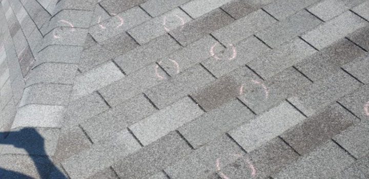 Close-up aerial shot of gray asphalt shingles with pink chalk circles marking hail impact points, indicating storm damage assessment by BN Exteriors inspectors.