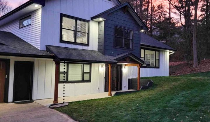 A modern two-story home with white and blue vertical siding is beautifully lit against a vibrant pink and purple twilight sky.
