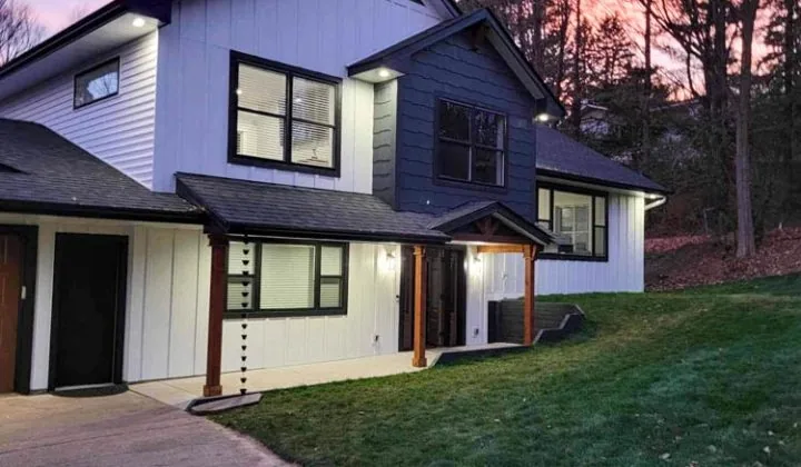 A modern two-story home with white and blue vertical siding is beautifully lit against a vibrant pink and purple twilight sky.