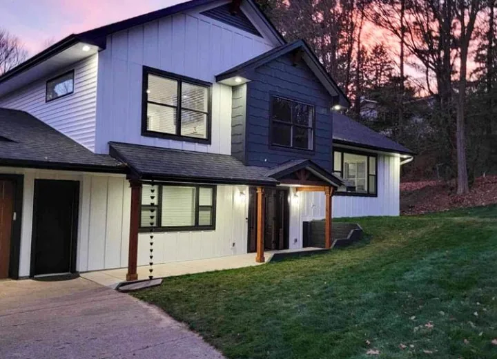 A modern two-story home with white and blue vertical siding is beautifully lit against a vibrant pink and purple twilight sky.
