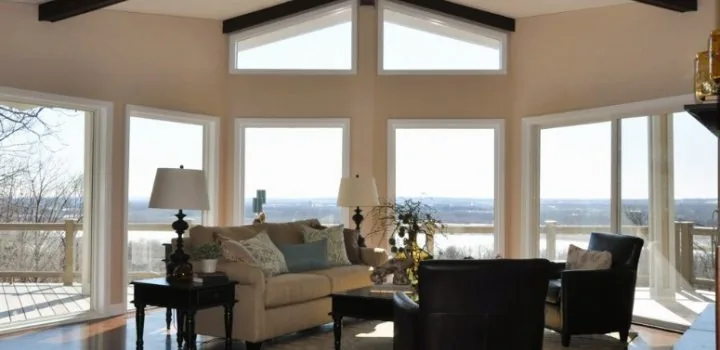 Spacious great room with exposed ceiling beams, triangular clerestory windows, and large rectangular windows offering a panoramic landscape view.
