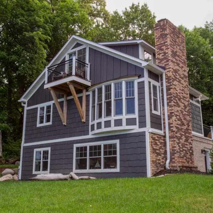 A stylish, multi-level home featuring dark gray horizontal siding, white trim, and a prominent brick chimney, nestled in a lush green landscape.