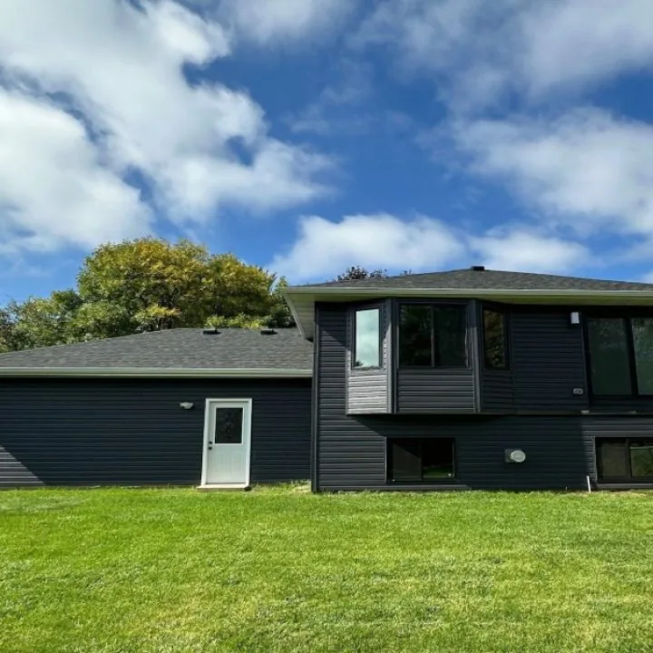 Backyard view of a mid-century modern home updated with charcoal gray vertical board-and-batten upper level and horizontal siding below, contrasting white door and bright blue sky.
