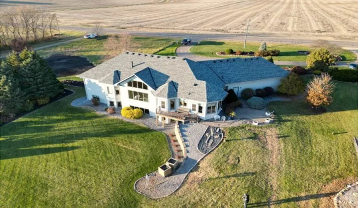 An aerial shot of a sprawling custom home with a gray roof, set on a large grassy lot next to open fields.