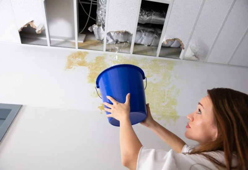 Worried Woman Holding A Blue Bucket Under The Leak Ceiling In Corridor
