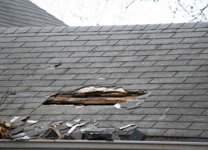 Roof of a residential house showing damage, multiple layers of shingles, missing shingles