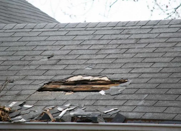 Roof of a residential house showing damage, multiple layers of shingles, missing shingles
