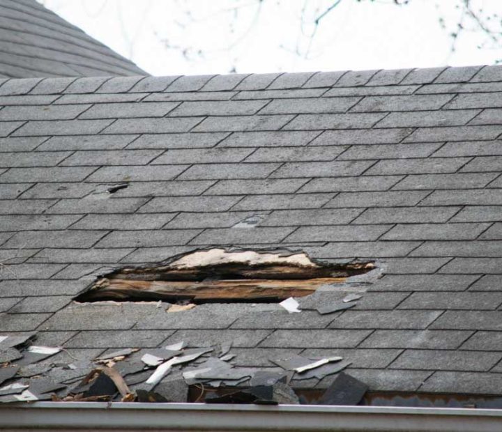 Roof of a residential house showing damage, multiple layers of shingles, missing shingles