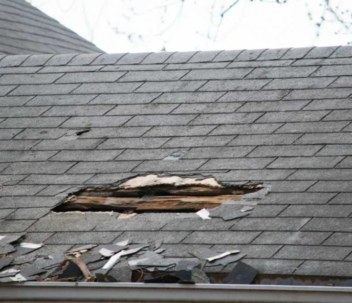 Roof of a residential house showing damage, multiple layers of shingles, missing shingles