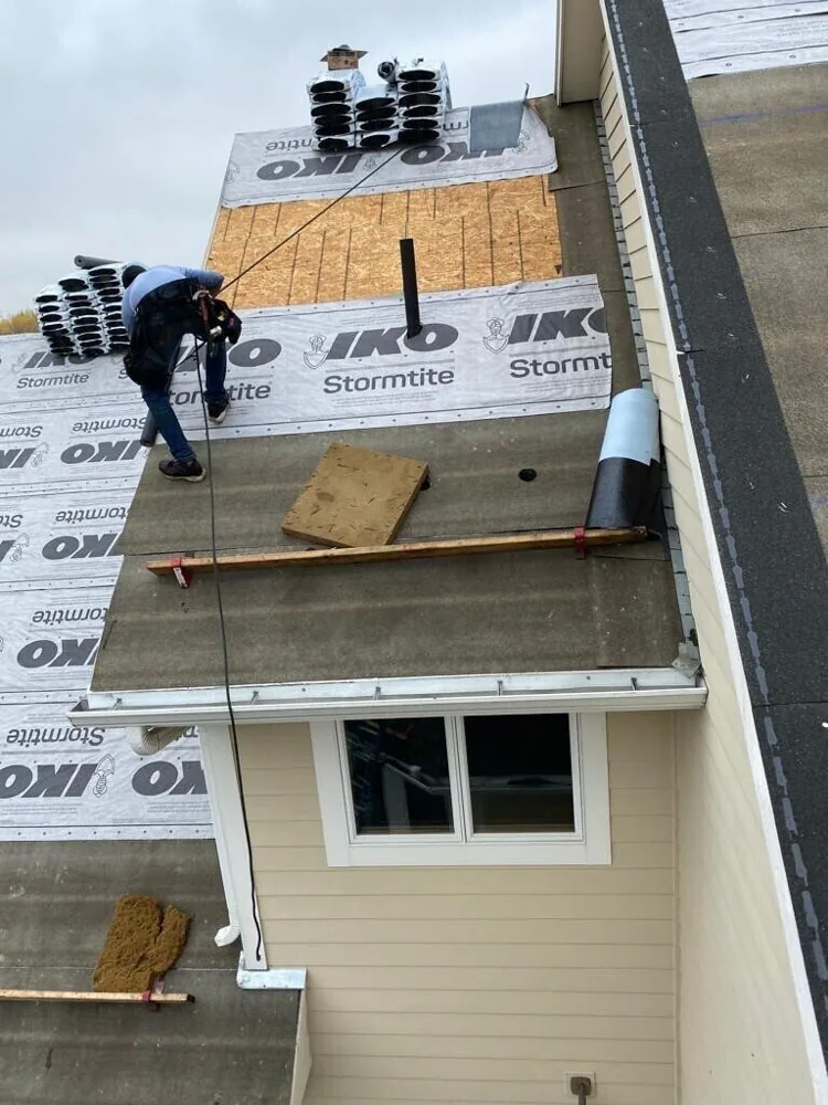 A BN Exteriors roofer fastening IKO Stormtite underlayment across a roof deck before new shingles go on