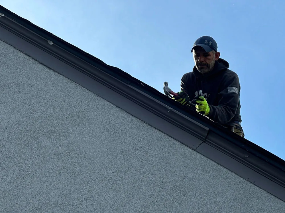 A BN Exteriors crew member working along the roof edge of a home, fastening trim at the gutter line