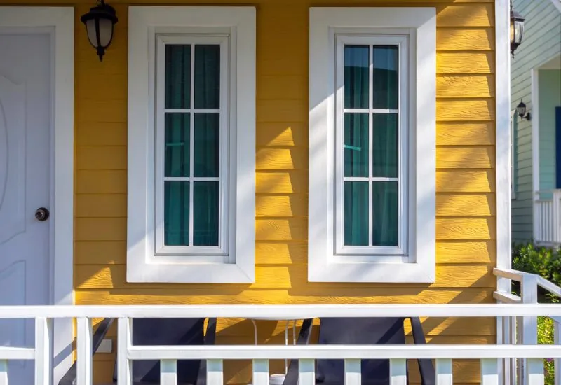 A house with installed wood siding painted yellow and two windows with white trims