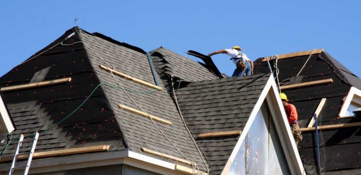 Construction workers putting shingles on the roof of a house.