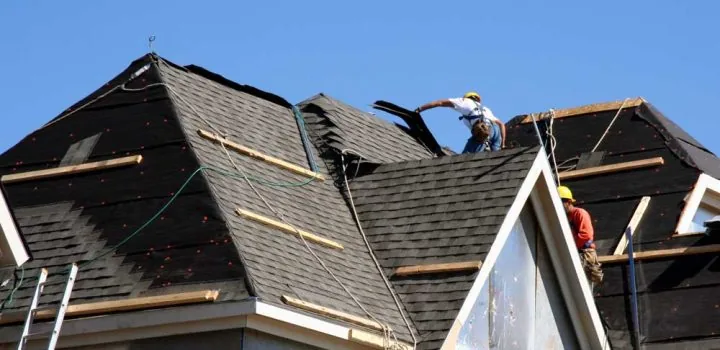 Construction workers putting shingles on the roof of a house.