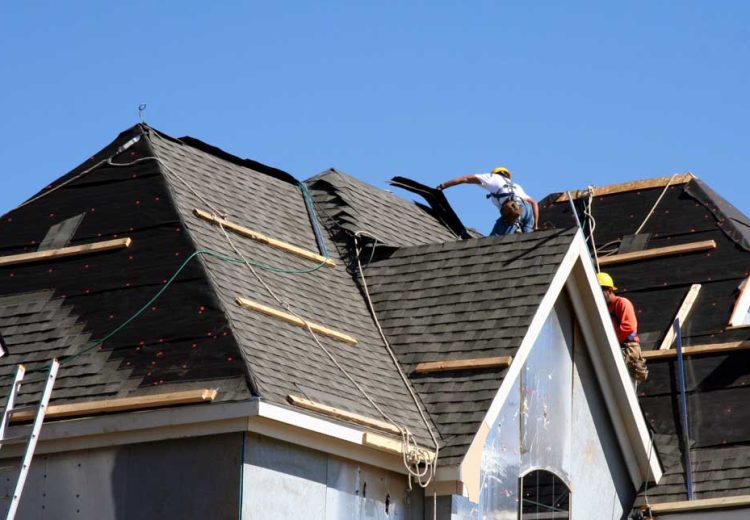 Construction workers putting shingles on the roof of a house.