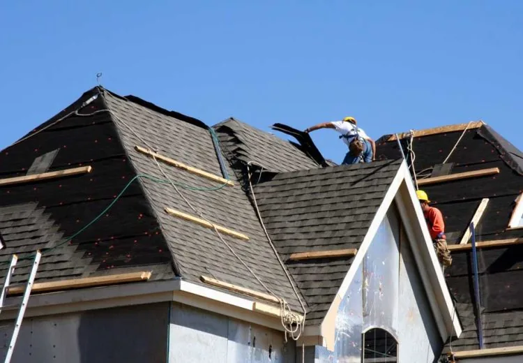 Construction workers putting shingles on the roof of a house.