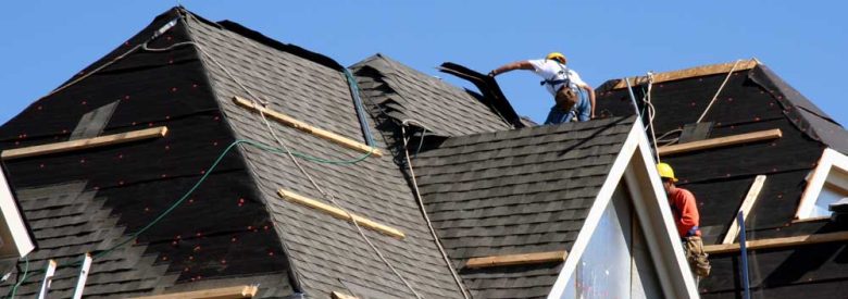 Construction workers putting shingles on the roof of a house.