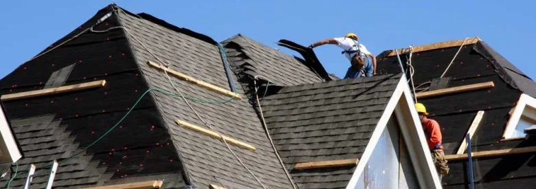 Construction workers putting shingles on the roof of a house.