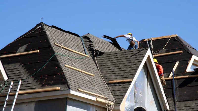 Construction workers putting shingles on the roof of a house.