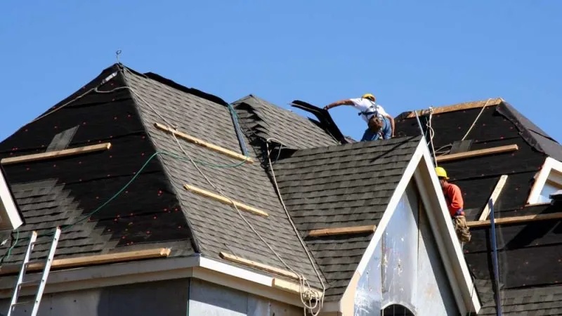 Construction workers putting shingles on the roof of a house.