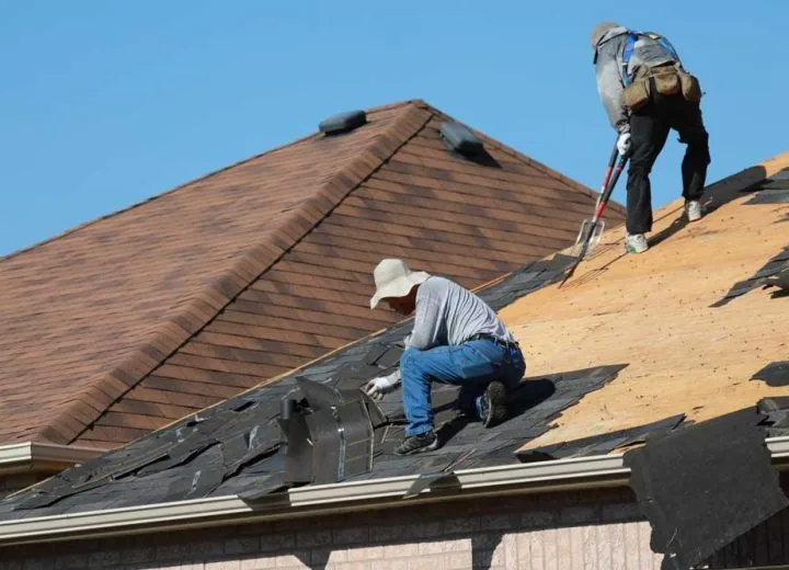 Roofers removing old asphalt shingles from the roof of a residential house