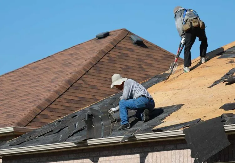 Roofers removing old asphalt shingles from the roof of a residential house
