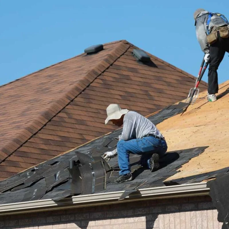 Roofers removing old asphalt shingles from the roof of a residential house