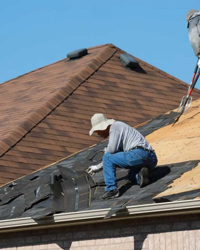 Roofers removing old asphalt shingles from the roof of a residential house