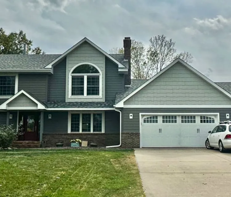 A view from the front yard of a house with a wide garage and concrete driveway, and a lawn