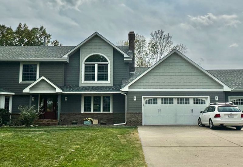 A view from the front yard of a house with a wide garage and concrete driveway, and a lawn
