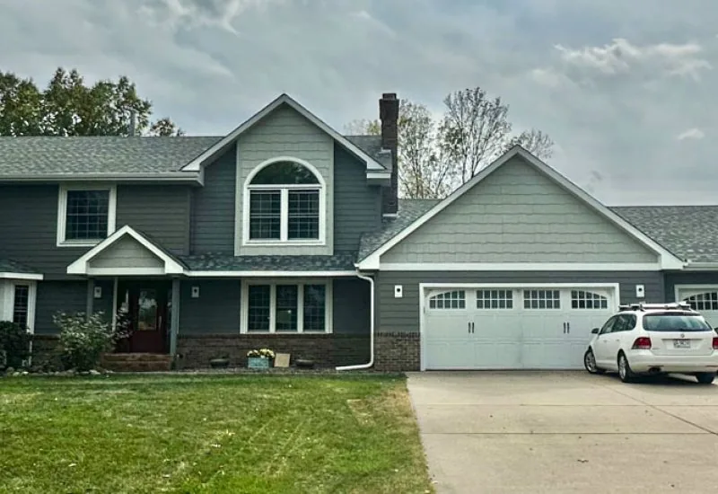 A view from the front yard of a house with a wide garage and concrete driveway, and a lawn