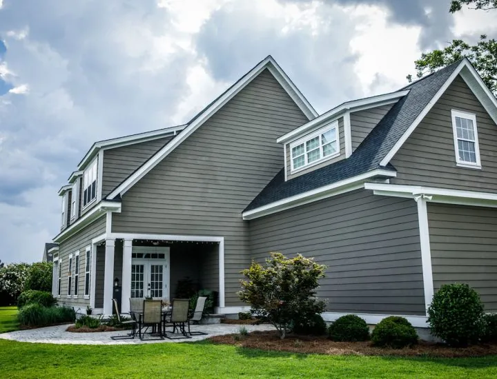 A large, elegant home with gray siding, white trim, and a covered patio under a dramatic cloudy sky.
