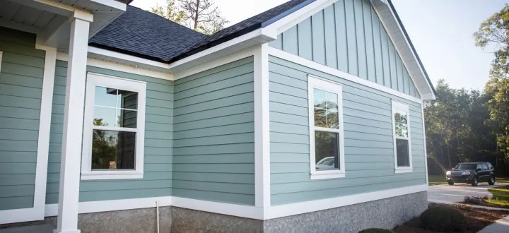The corner of a newly finished home with light blue siding, crisp white trim, and a textured stone foundation.