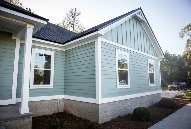 The corner of a newly finished home with light blue siding, crisp white trim, and a textured stone foundation.