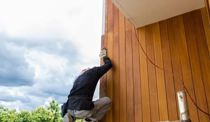 A skilled worker installing siding using Fiber Cement Board on the exterior wall of a property