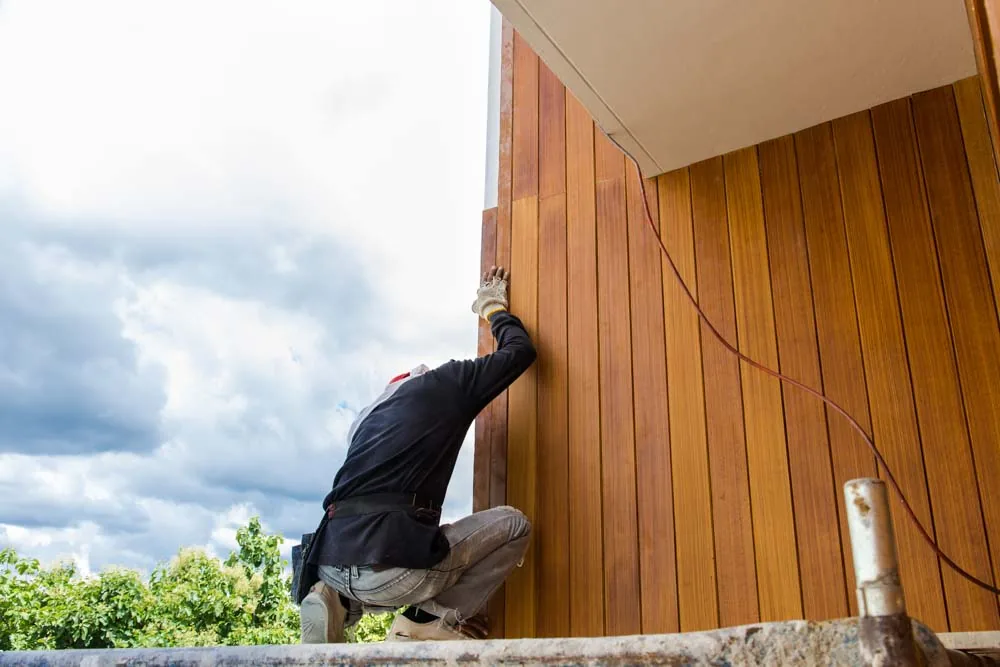 A skilled worker installing siding using Fiber Cement Board on the exterior wall of a property