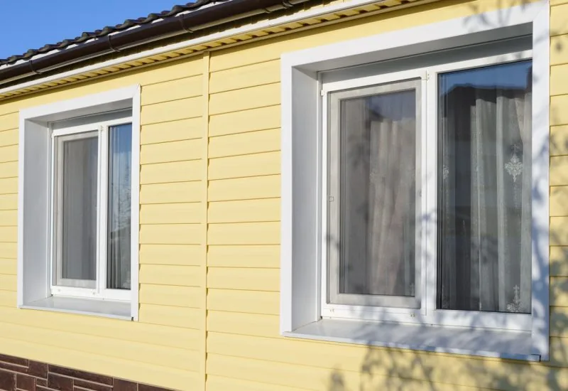 A detailed shot of newly installed white vinyl windows on a yellow-sided house, showcasing clean lines and modern design.
